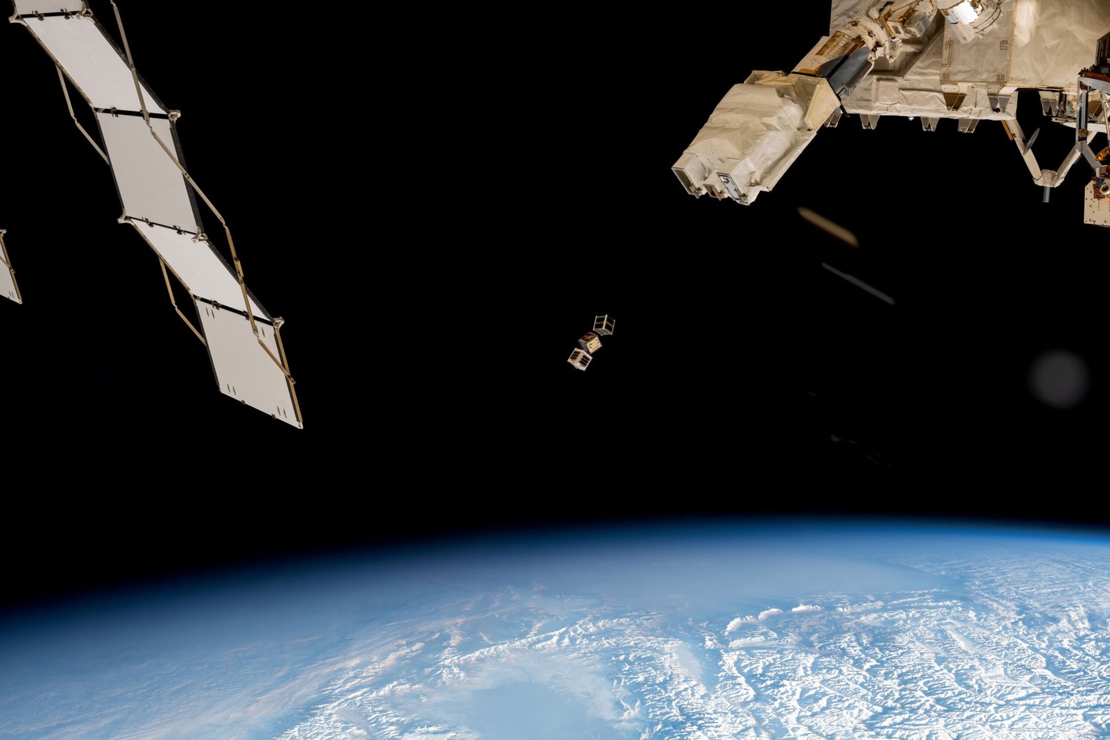 A trio of CubeSats in Earth orbit, seen against the blackness of space.
